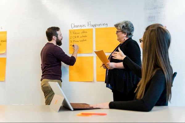 Man writing on whiteboard as female colleagues look on